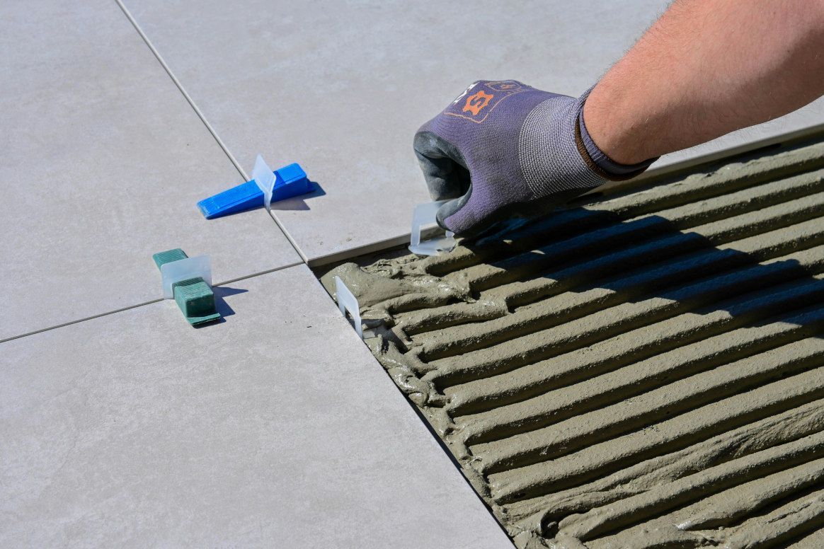 A person tiling with leveling clips and wedges, with a gloved hand placing the clip between tiles.