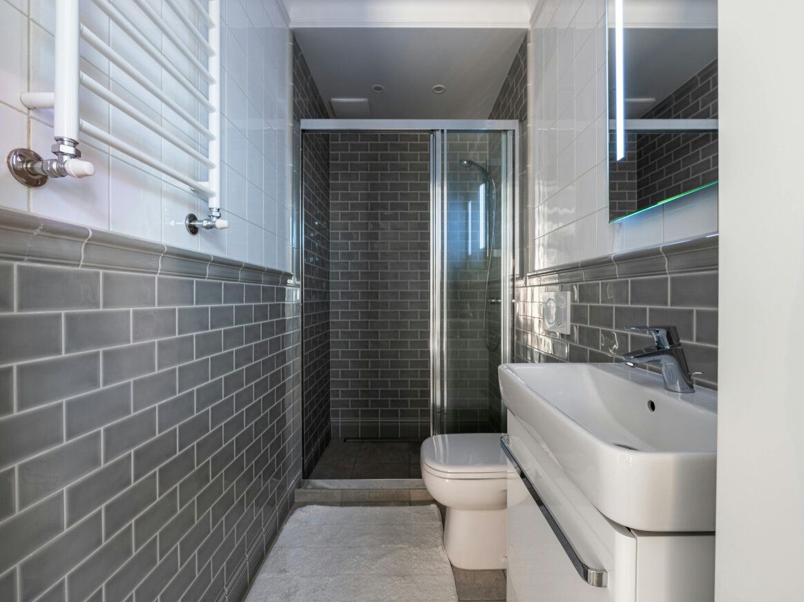Small, modern bathroom with gray subway tile walls, a shower, toilet, and sink.