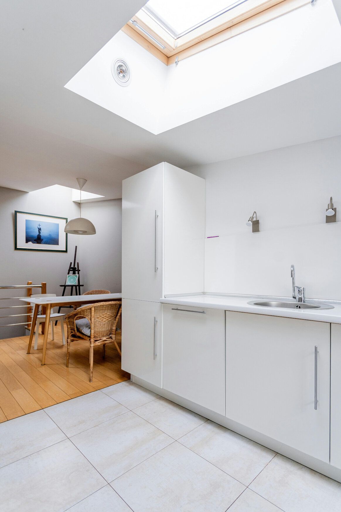Bright kitchen with white cabinets, skylight, and dining area with framed art.
