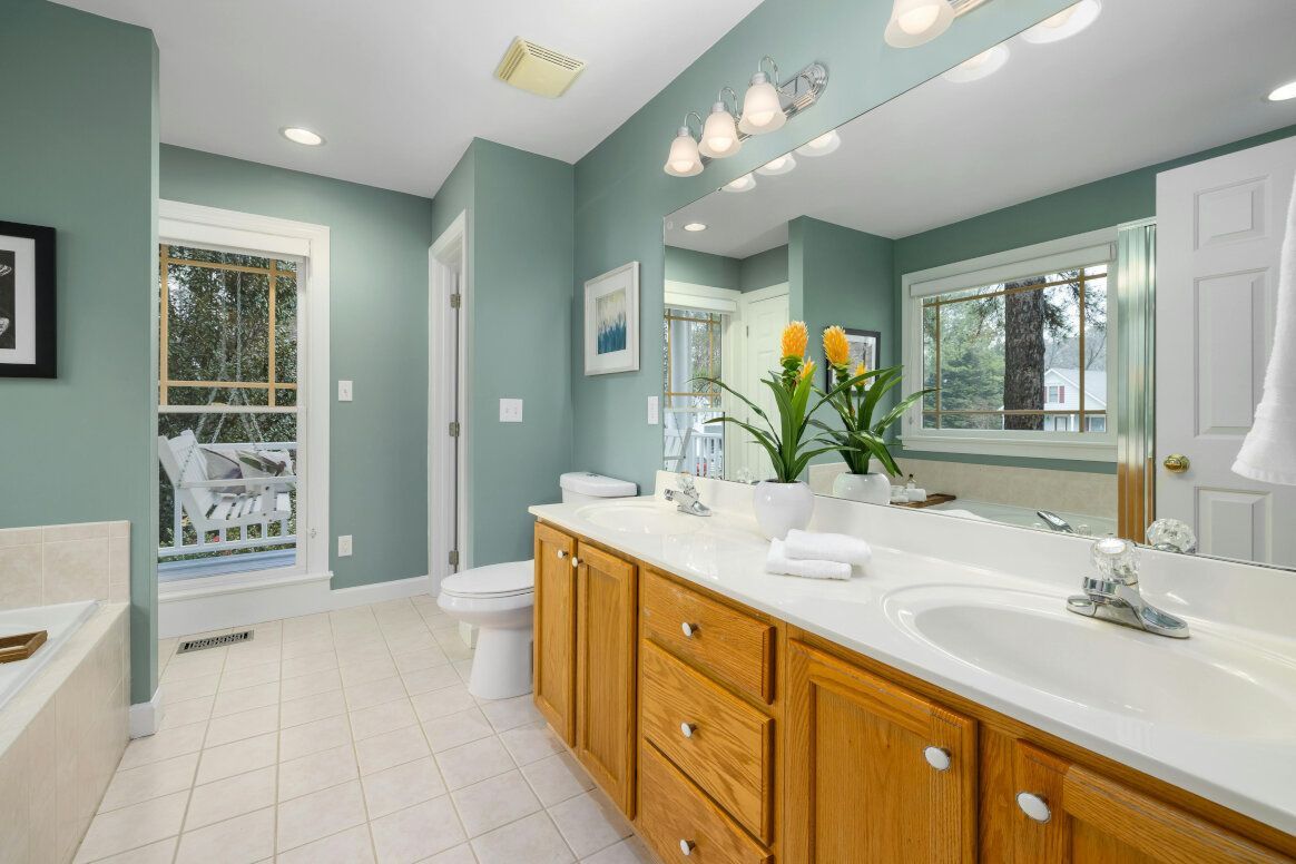 Bathroom with wooden cabinets, teal walls, white sink, and a view of the outdoors.