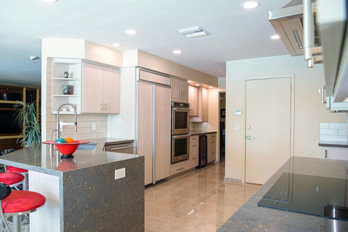 Modern kitchen with island, light cabinets, stainless steel appliances, and red bar stools.