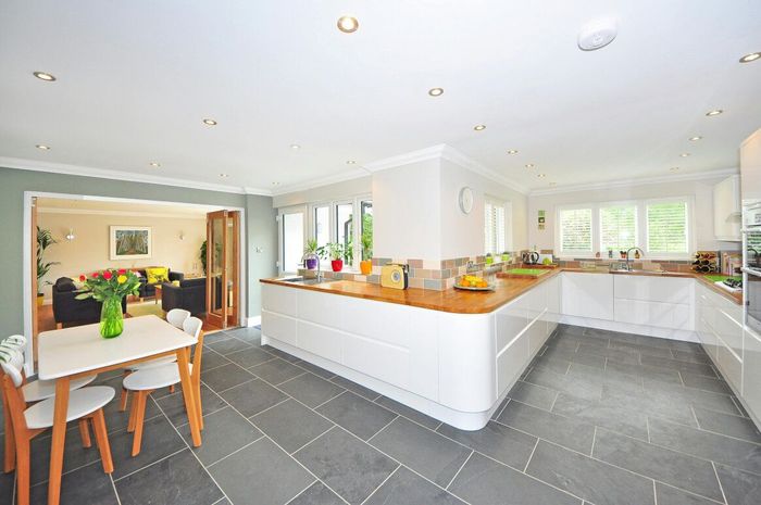 Bright, modern kitchen with white cabinets, wood countertops, and slate tile floor. Dining area and living room visible.