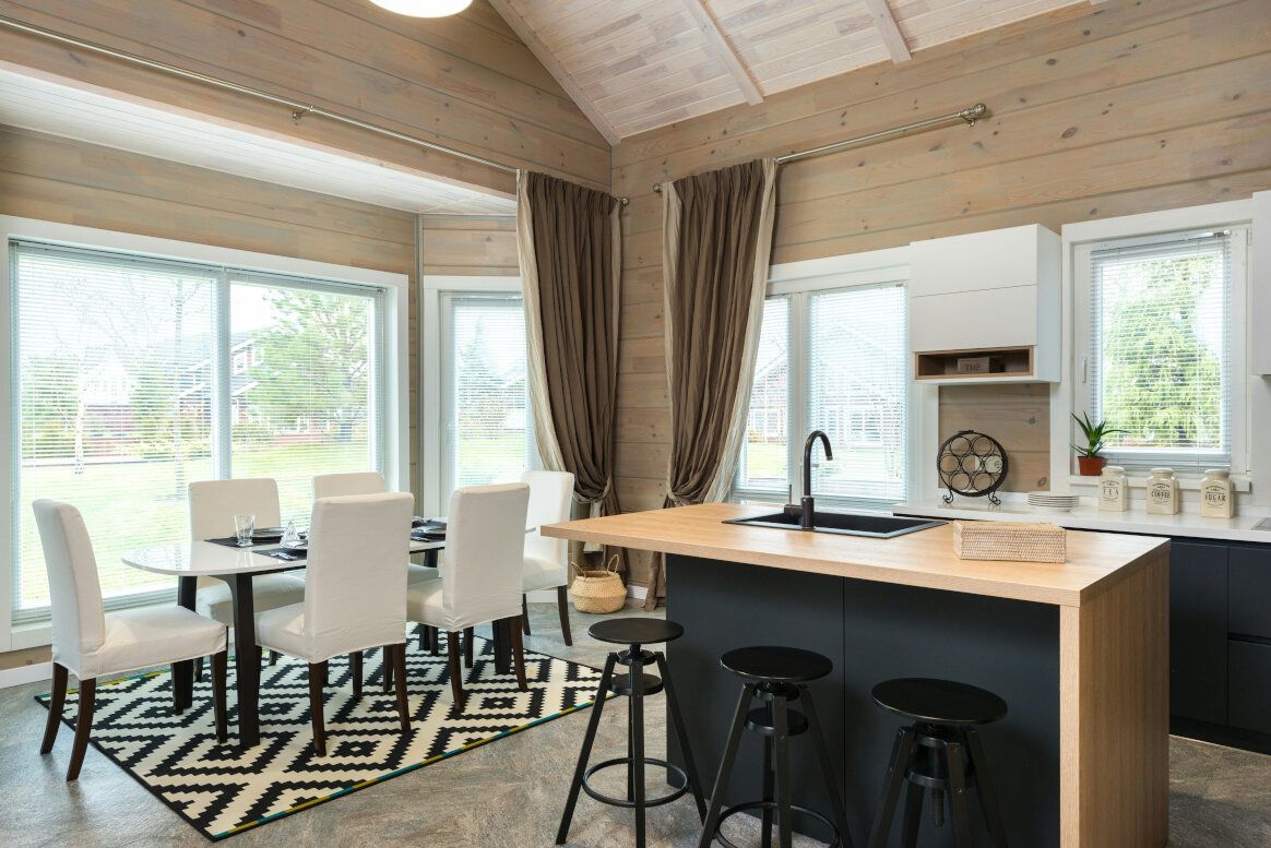 A light-filled kitchen with dining area. Features include a black island, round table, and patterned rug.