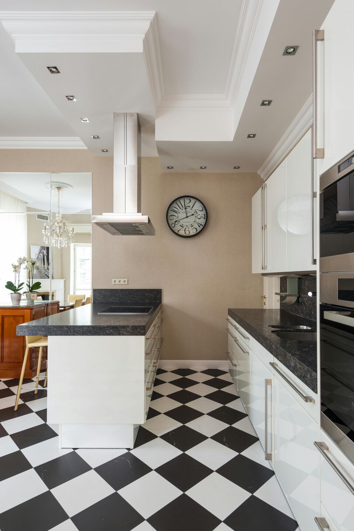 Black and white checkered floor, white cabinets, black countertops, stainless steel range hood, and clock in a kitchen.