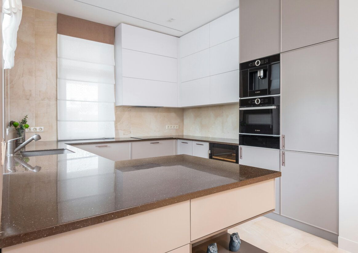 Modern kitchen with light beige and brown cabinetry, appliances, and a large countertop.