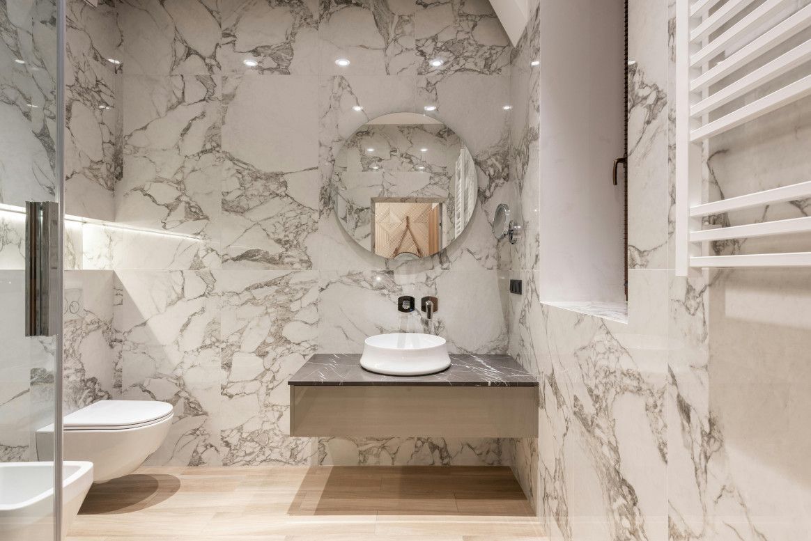 Luxurious bathroom with white marble walls, floating vanity, and round mirror.