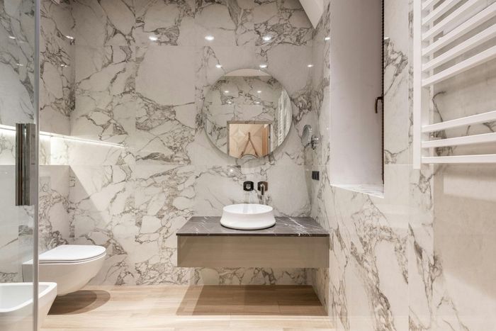 Luxurious bathroom with white marble walls, floating vanity, and round mirror.