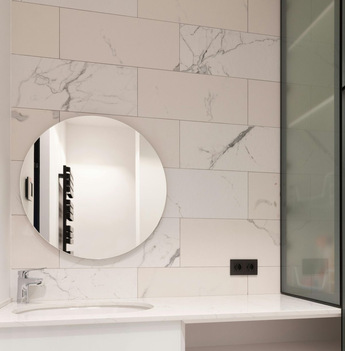 Round mirror over a marble-tiled vanity in a modern bathroom.