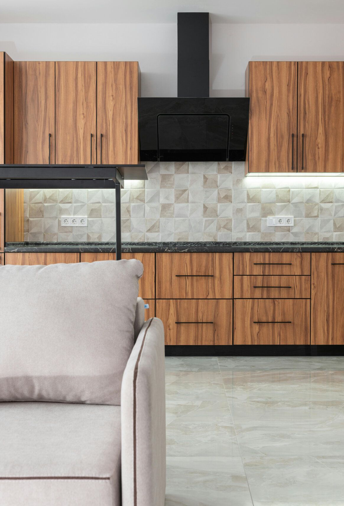 Cozy kitchen with wood cabinets, a black range hood, and a beige sofa.