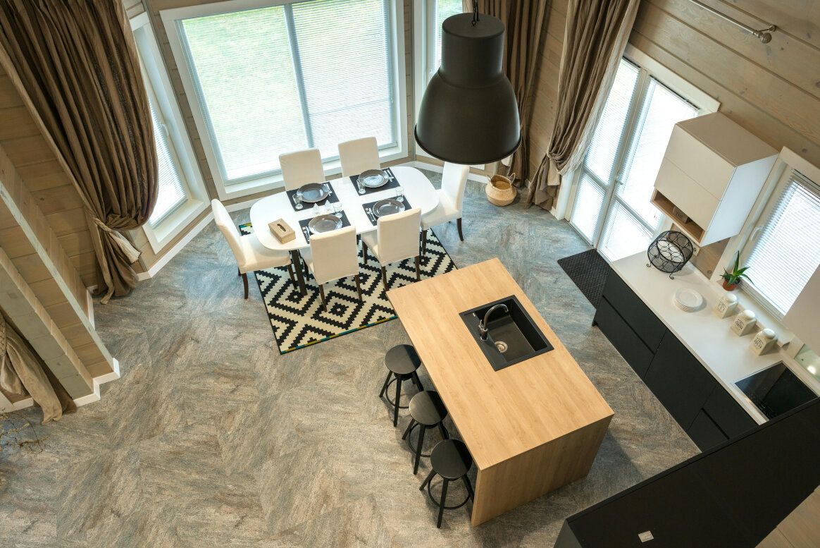 High-angle view of a modern kitchen and dining area with light wood accents, black and white rug, and large windows.