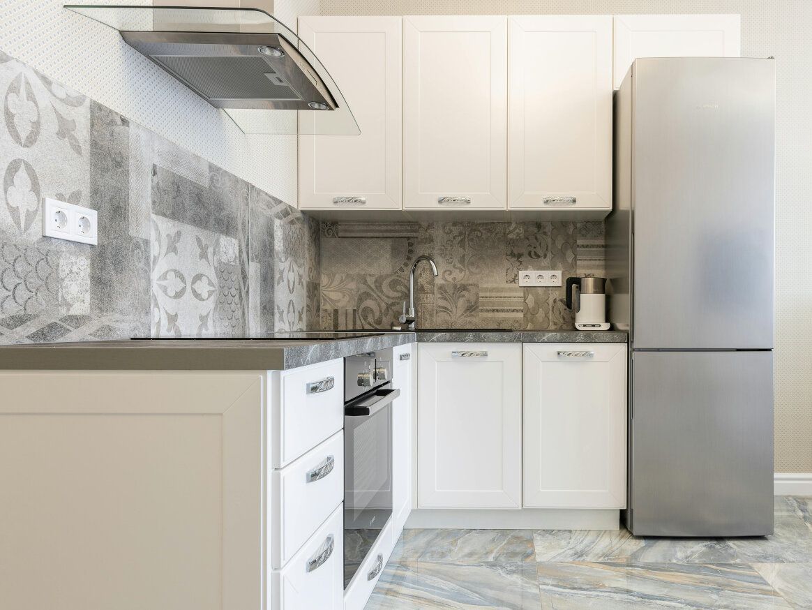 White kitchen with gray backsplash, stainless steel appliances, and gray countertop.