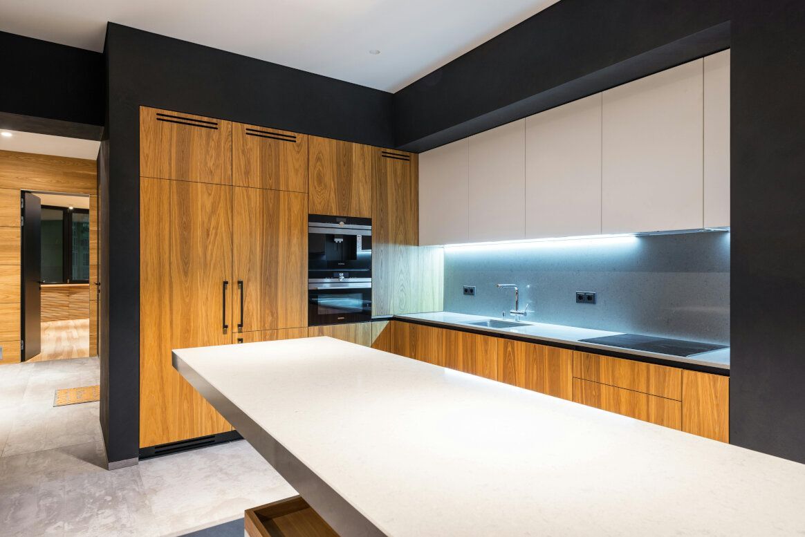 Modern kitchen with wood cabinets, white countertops, and a black wall.