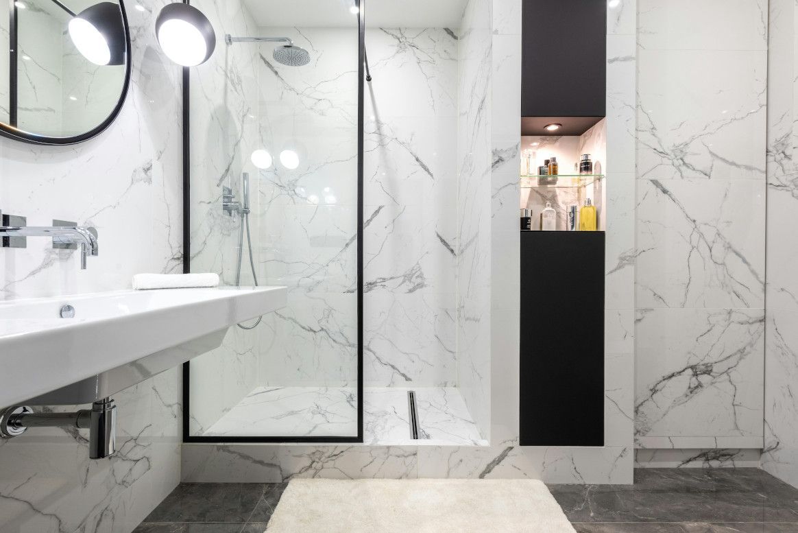 Modern white marble bathroom with glass shower, black accents, and built-in storage.