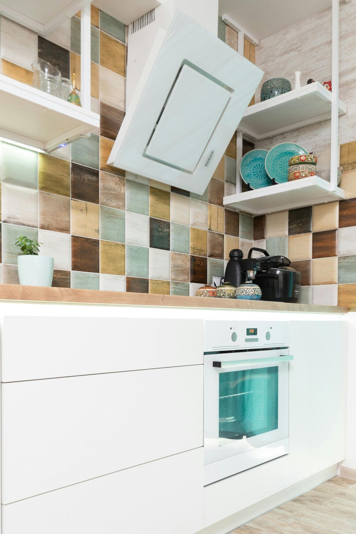 White modern kitchen with oven, vent hood, tiled backsplash, and open shelving.
