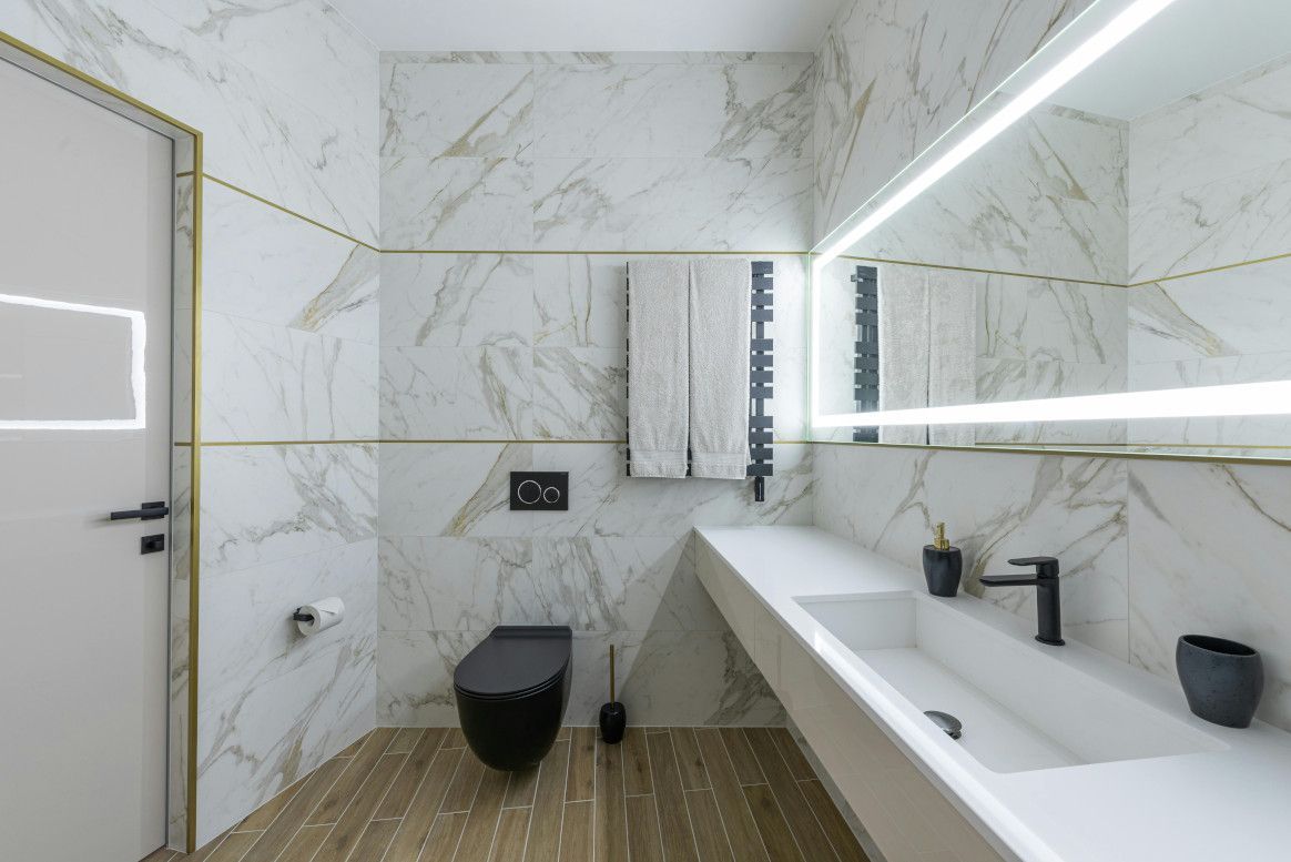 Modern bathroom with white marble tiles, black toilet, and floating sink.