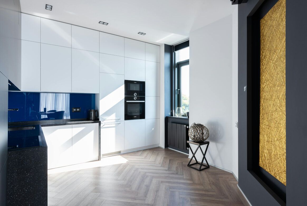 Modern white kitchen with blue backsplash, dark countertops, and herringbone floor; a gold accent wall.