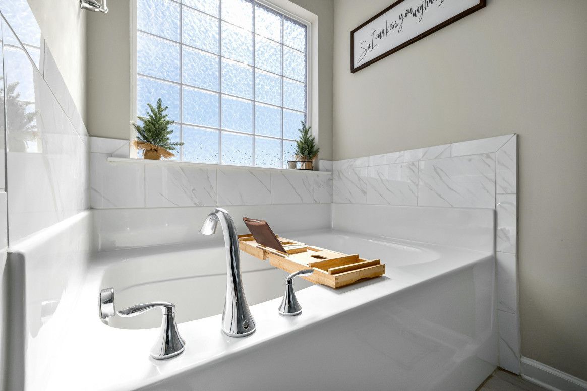 Bright bathroom with white tub, marble wall, window, and wooden bath tray.