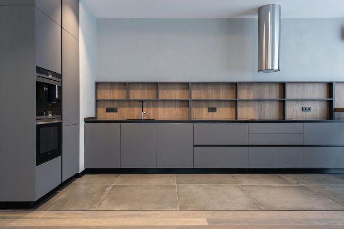 Modern kitchen with grey cabinets, wooden shelving, and stainless steel hood.