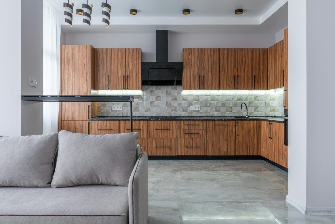 Kitchen with wood cabinets, black countertops, and a neutral-colored sofa.