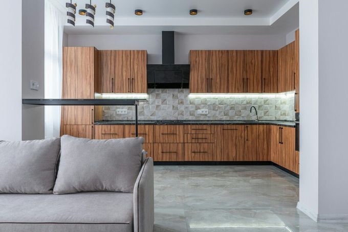 Modern kitchen with wood cabinets, black countertops, and a gray sofa.