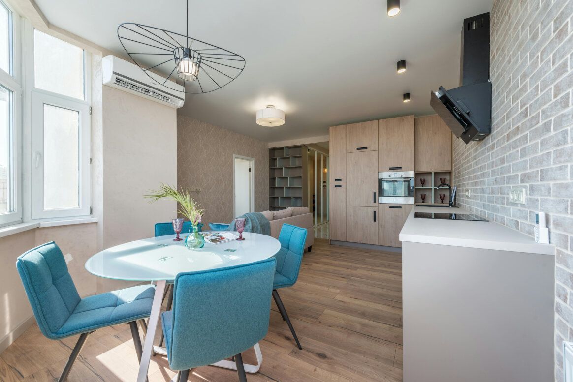 Small modern kitchen with a dining area, featuring blue chairs and light wood cabinets.