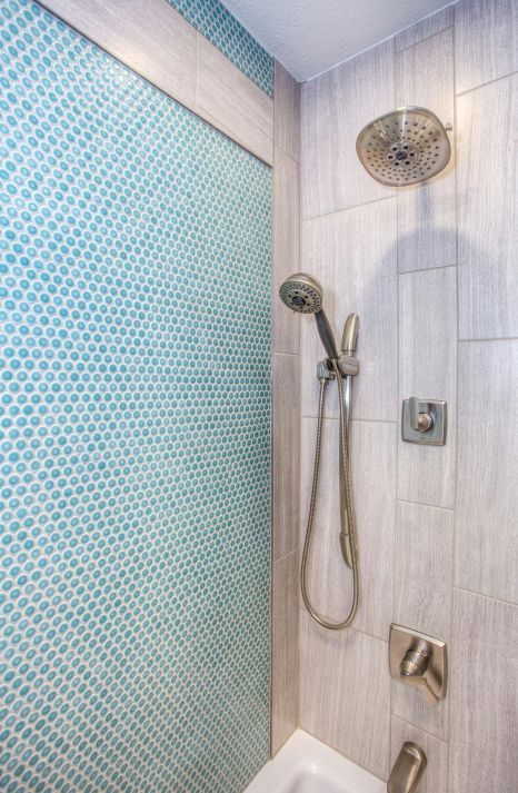 A shower with a blue tile wall and a shower head. Expertly tiled by Daffodil Tiling in Swansea, Wales.