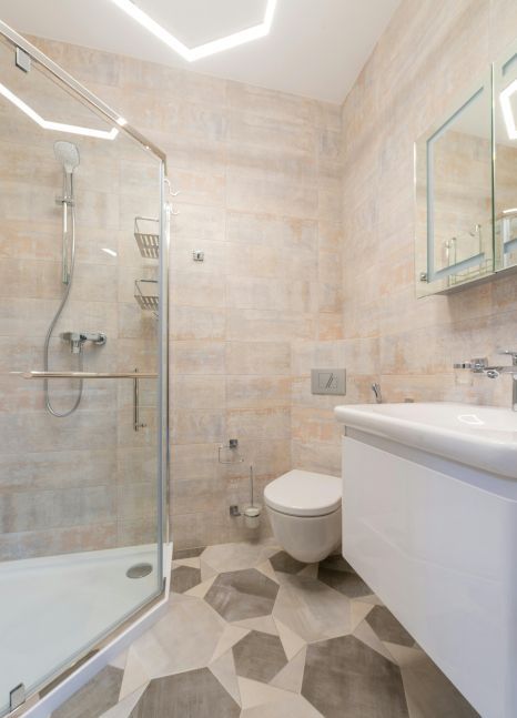 A bathroom with a toilet , sink , shower and mirror. Expertly tiled by Daffodil Tiling in Swansea, Wales.