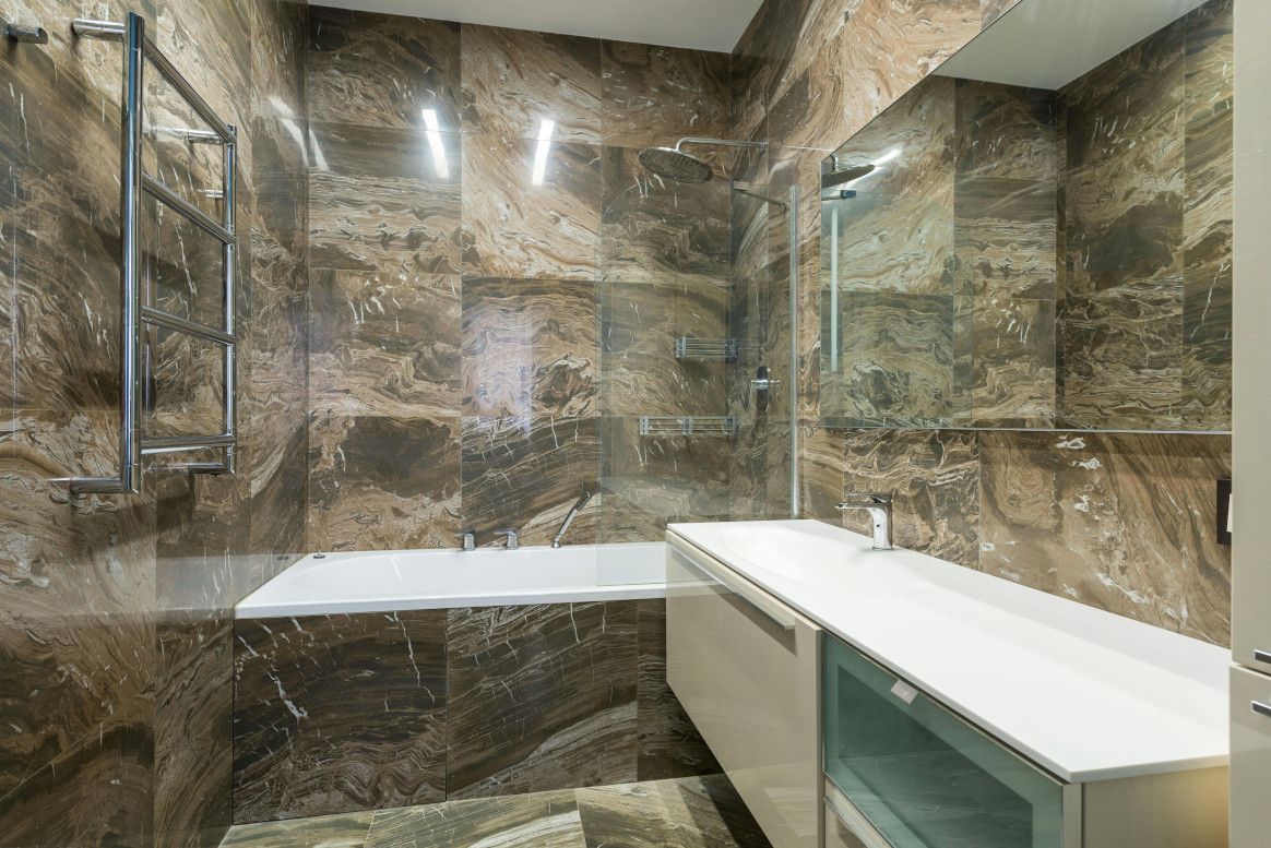 Modern bathroom with marble walls, a bathtub, and a long white vanity.