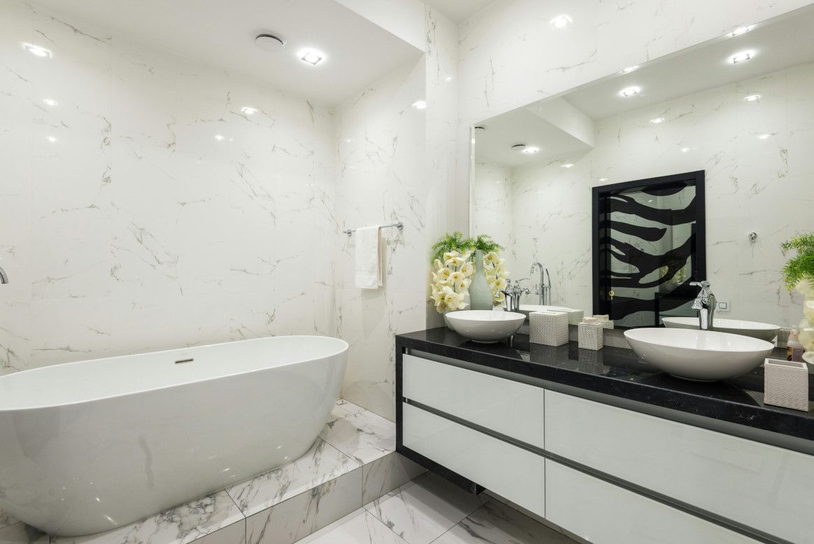 Modern white bathroom with freestanding tub, double sinks, and marble accents.
