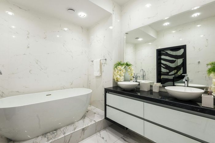 Modern white bathroom with a bathtub and vanity, featuring marble walls and dark counter.