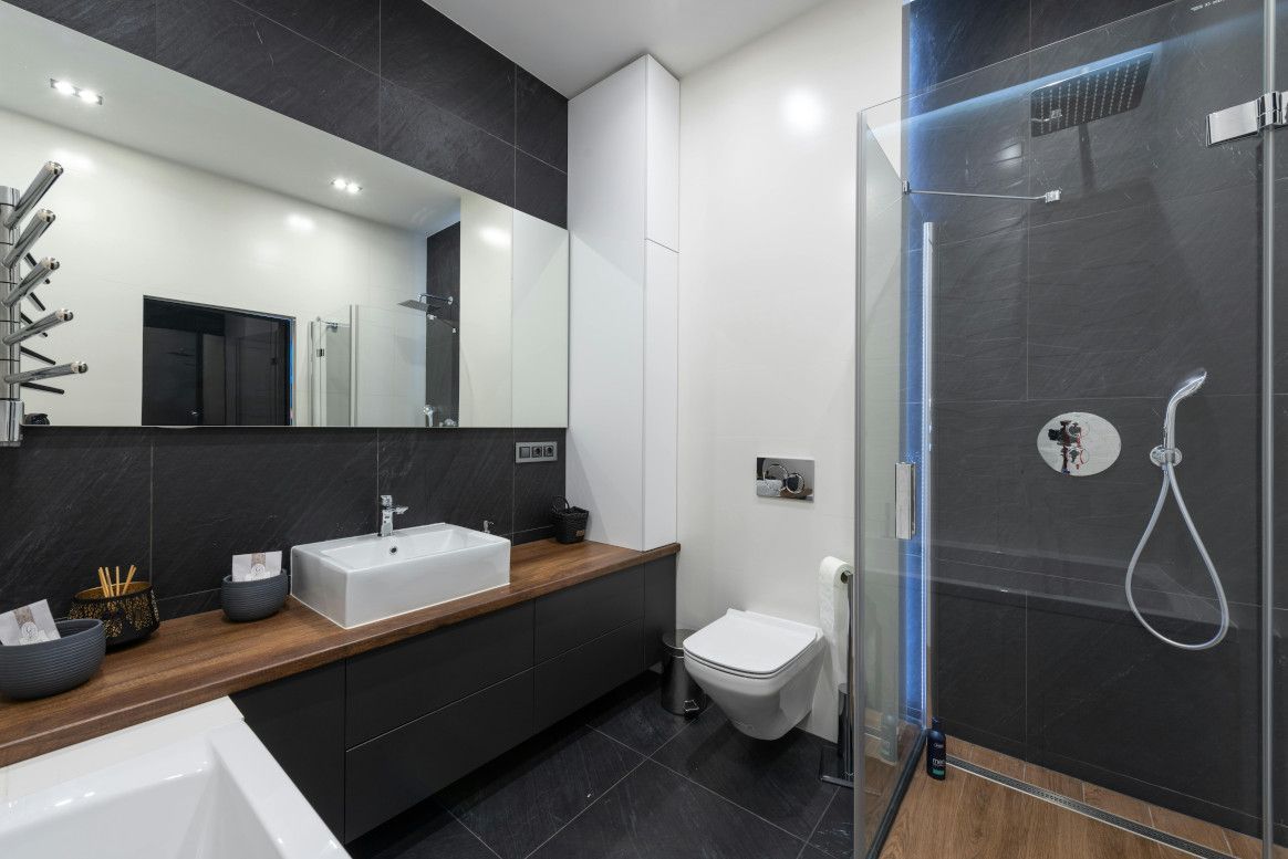 Modern bathroom with dark gray and white tiles, a wooden vanity, and a glass shower.