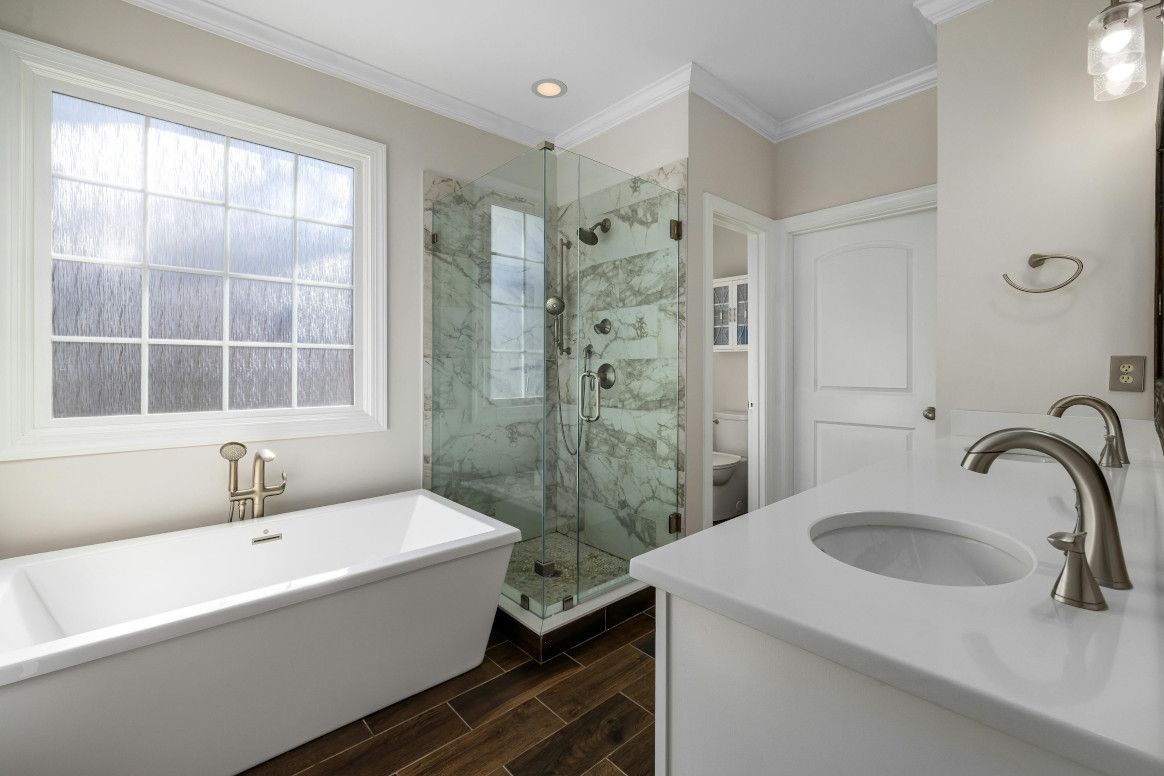 Bathroom with white vanity, tub, glass shower, and large window.