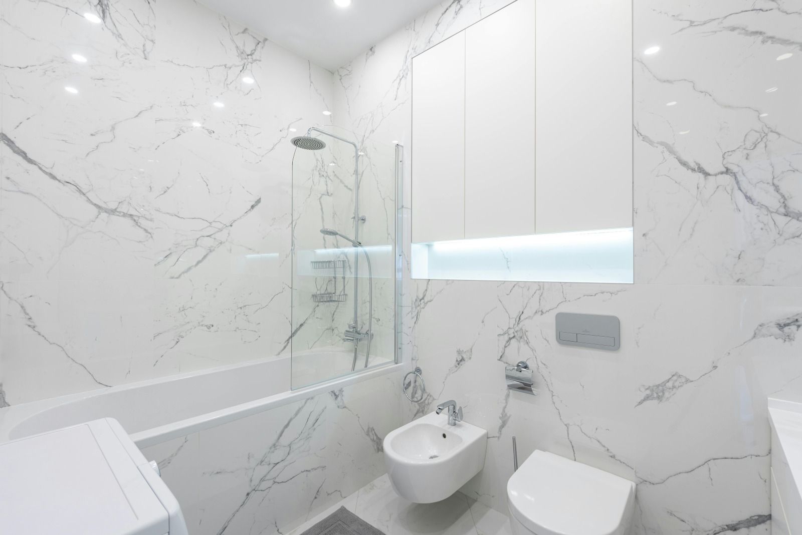 White marble bathroom with bathtub, shower, bidet, toilet, and window with a closed blind.