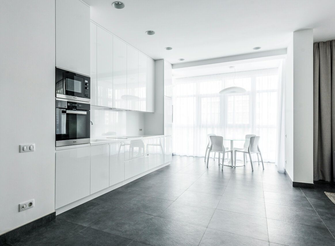 Modern white kitchen with dark flooring, natural light, and a small dining table.