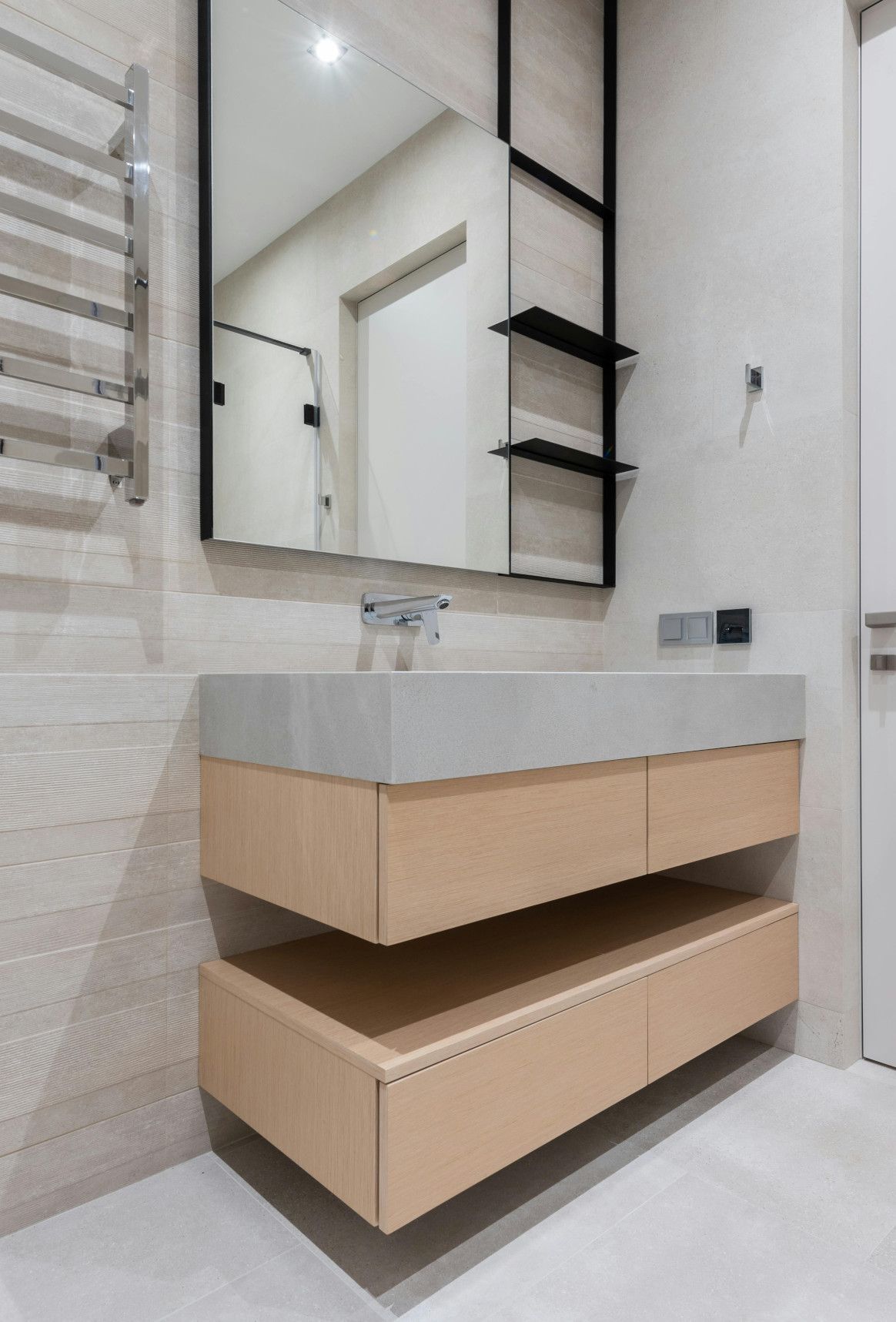Light wood bathroom vanity with concrete countertop, mirror, and shelving.
