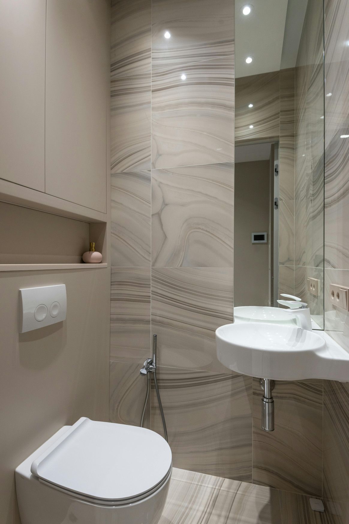 Modern bathroom with a white toilet, sink, and beige walls.