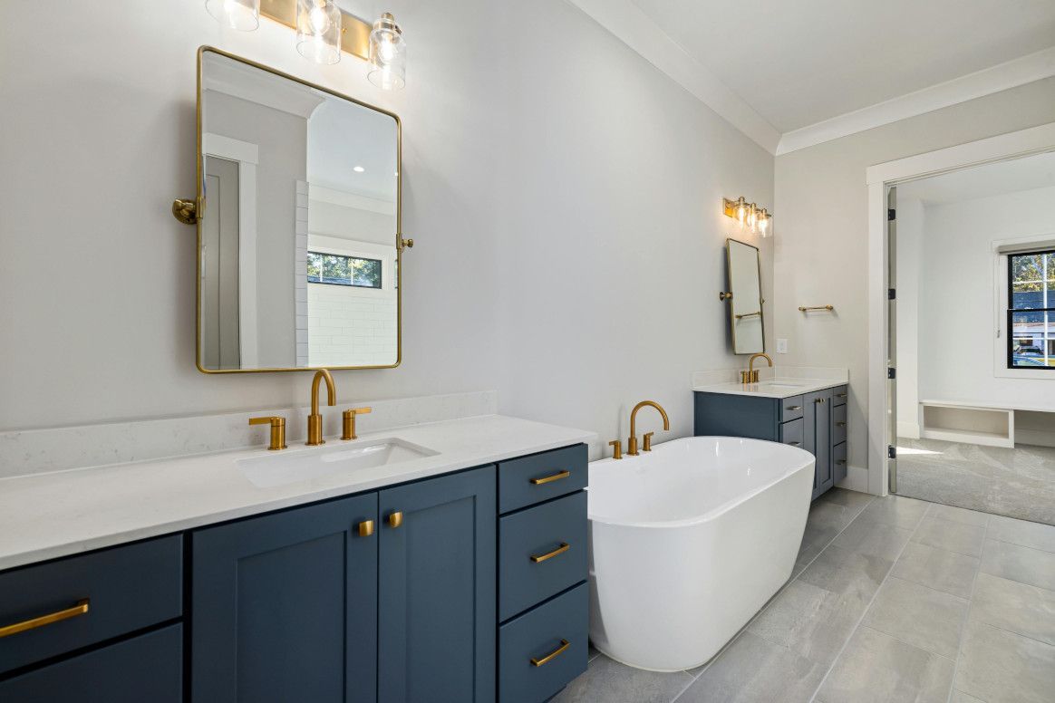 Spacious bathroom with blue cabinets, gold fixtures, white tub, and large mirror.