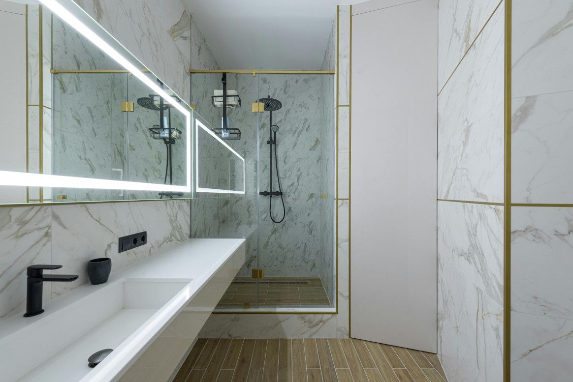 Modern bathroom with marble walls, gold trim, glass shower, and floating sink.
