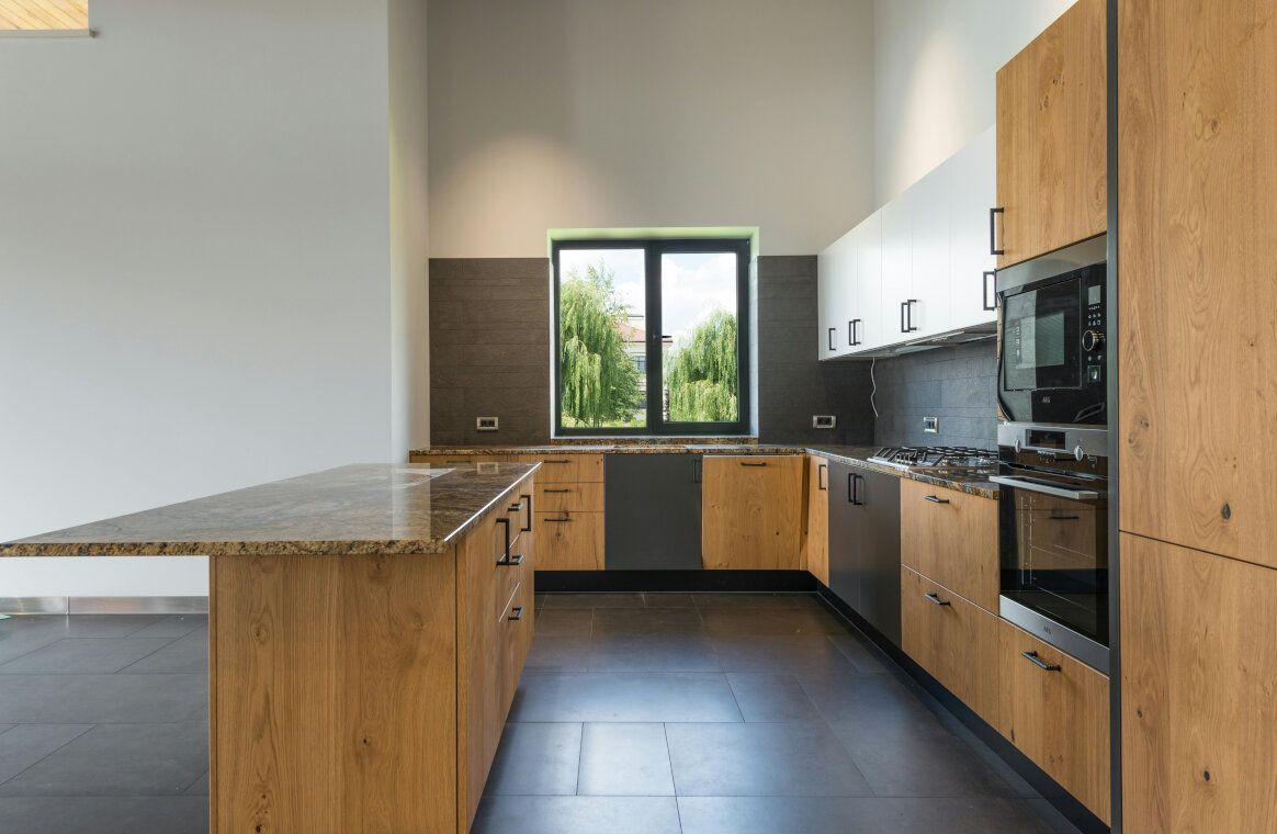 Modern kitchen with wooden cabinets, granite countertop island, and window overlooking trees.