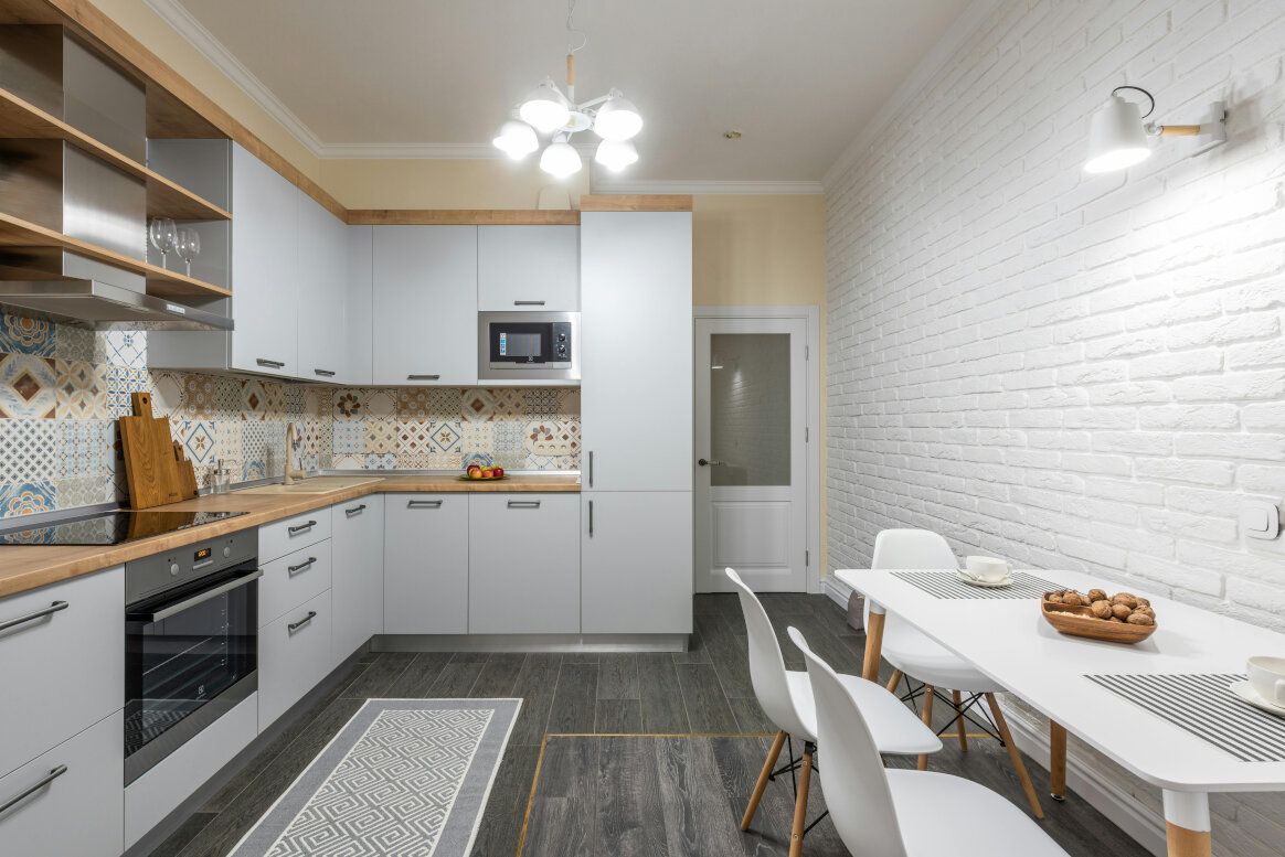 Modern kitchen with gray cabinets, white brick wall, and a dining table.