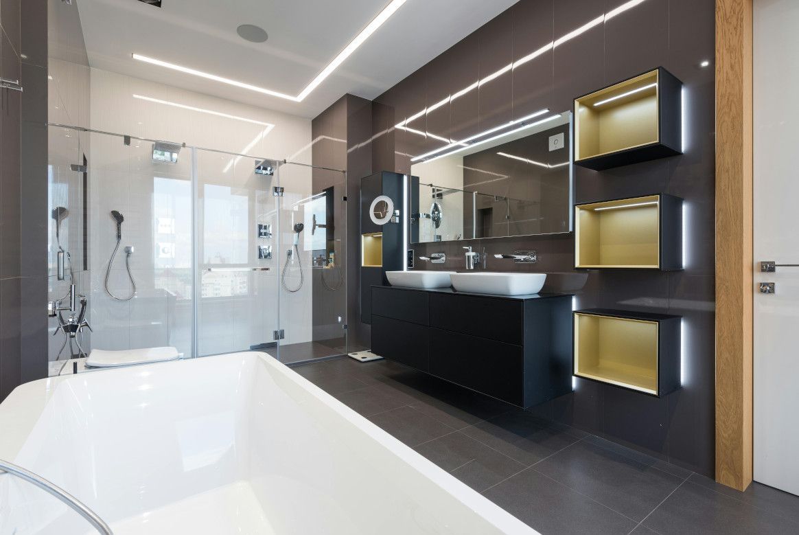 Modern bathroom with gray tile, white tub, glass shower, black vanity, and gold accents.