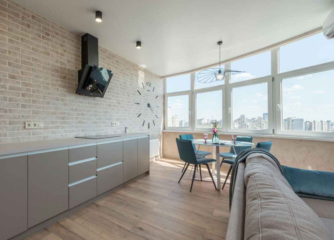Modern kitchen and dining area with light brick wall, gray cabinets, and large windows.
