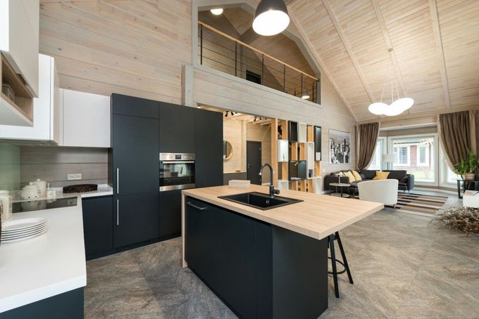 Modern open-plan kitchen with a black island, light wood cabinets, and a mezzanine level.