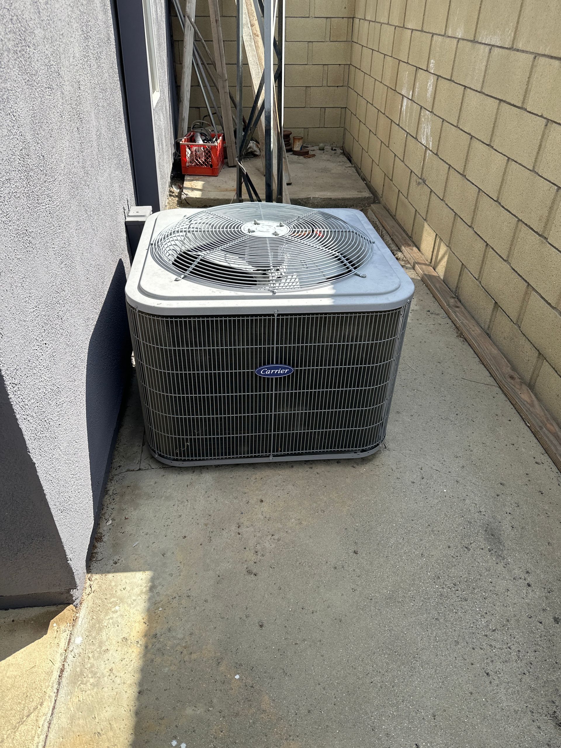 A large air conditioner is sitting on the sidewalk next to a brick wall.