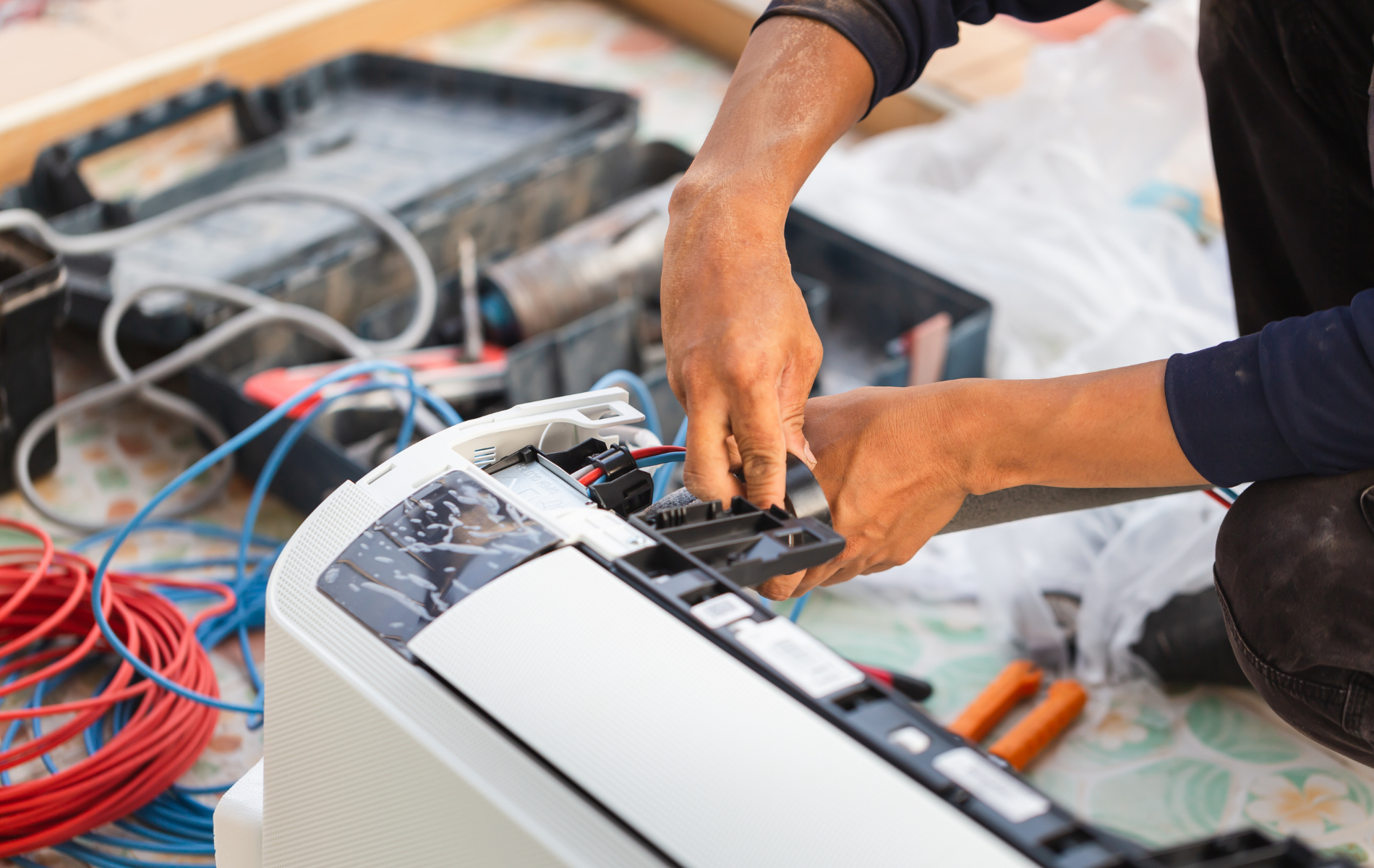 A man is sitting on the floor fixing an air conditioner.