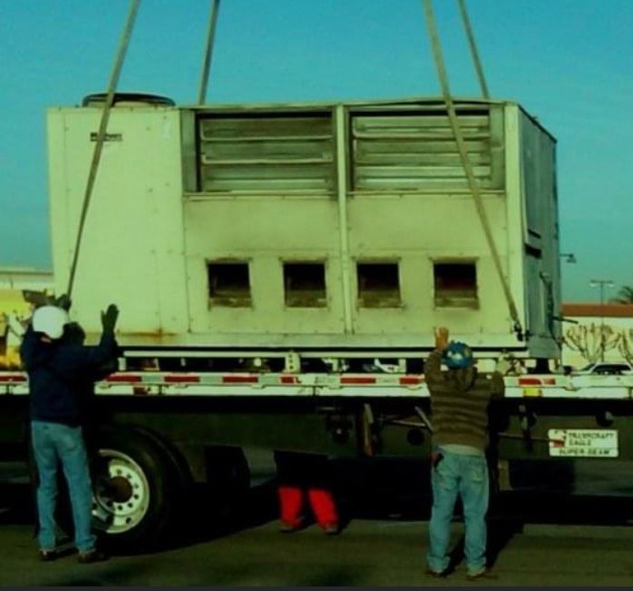 Two men are lifting a large white box on the back of a semi truck
