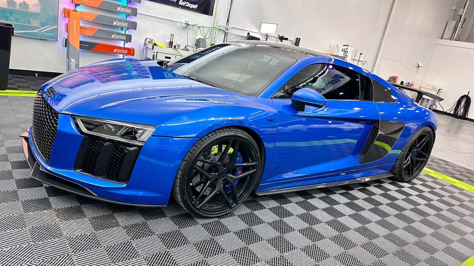 A blue audi r8 is parked on a checkered floor in a garage.
