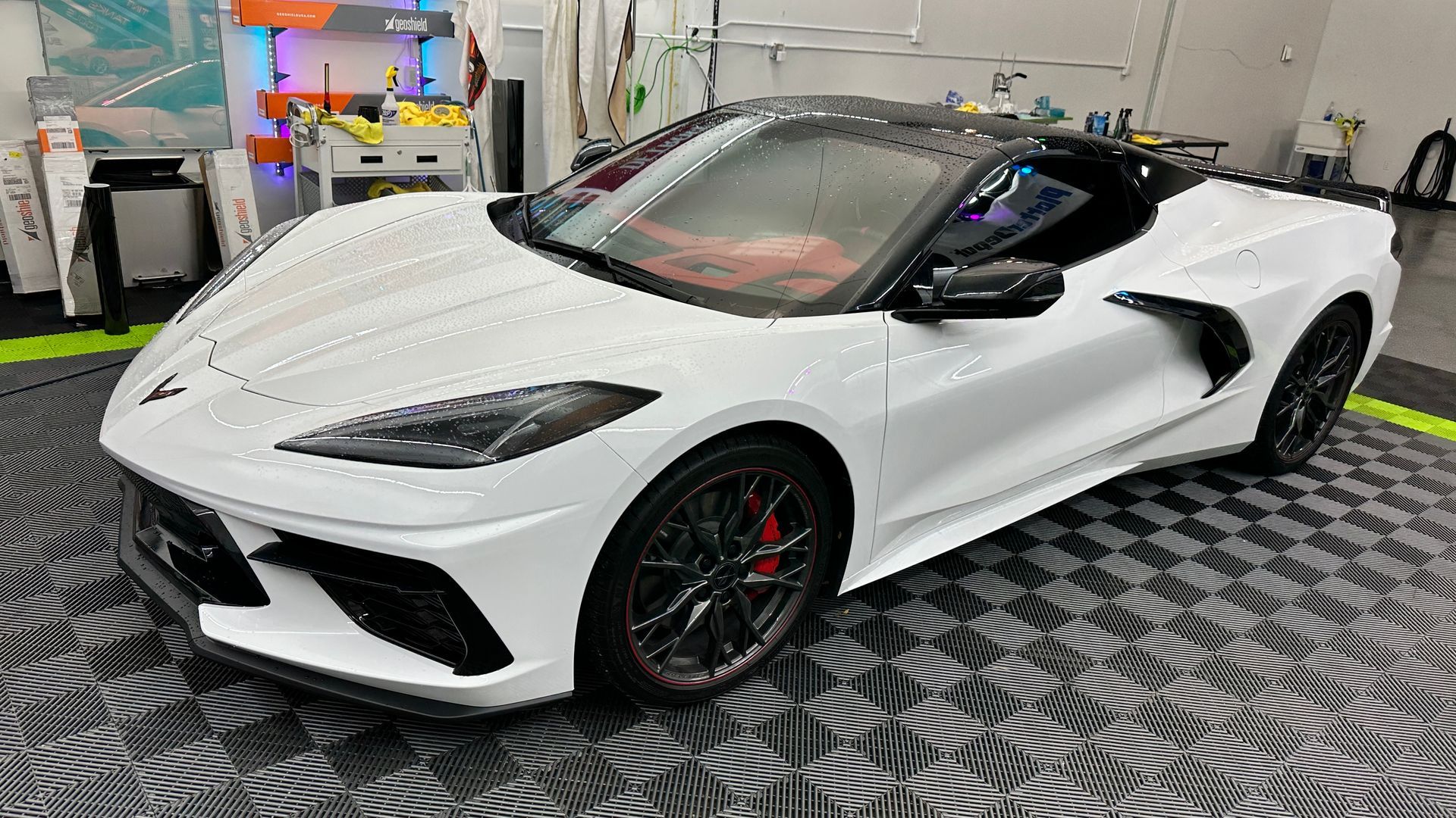 A white sports car is parked on a checkered floor in a garage.