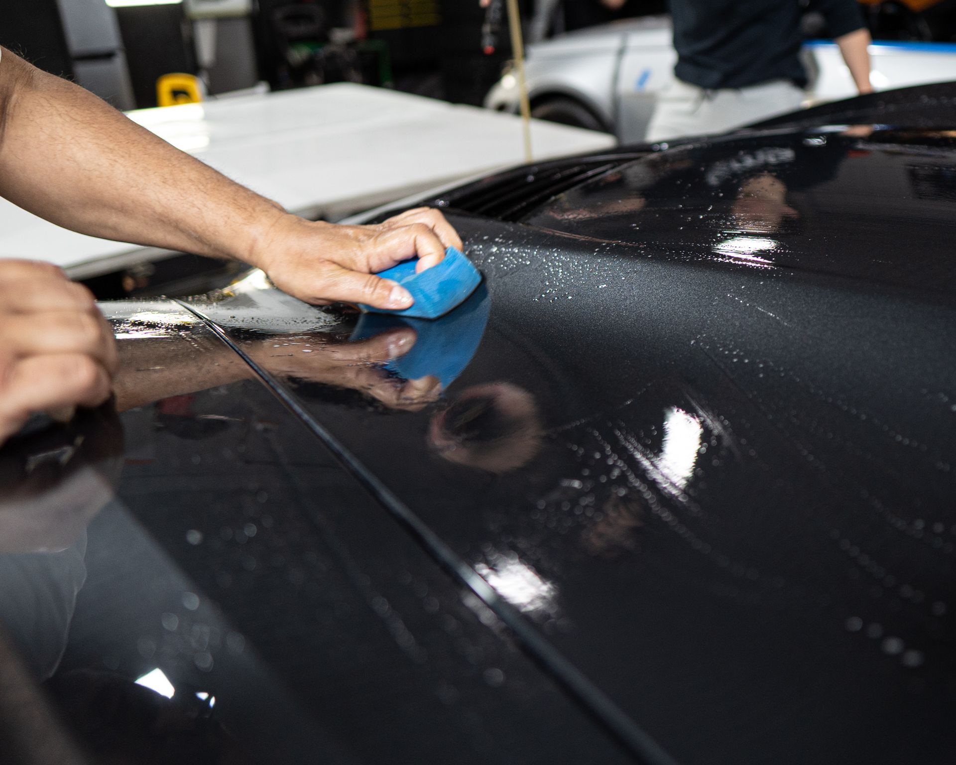 A person is cleaning the hood of a black car with a blue sponge.