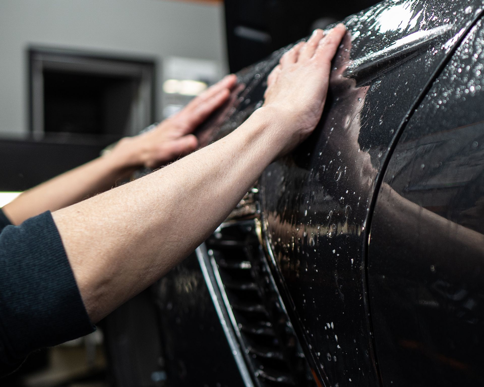 A person is applying a protective film to a black car.